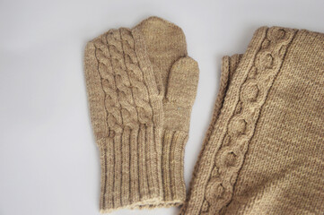 A pair of knitted wool beige mittens with a warm scarf on a white background. Winter accessories.