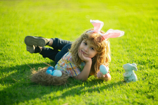 Easter kid in park. Bunny boy hunting eggs in park, Funny little Easter bunny child hunt easter eggs laying on grass in backyard. Easter kids portrait outdoor.