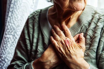 Elderly woman experiencing chest pain, clutching her heart with a look of concern. Close-up of an older woman's hands on chest feeling pain. - obrazy, fototapety, plakaty