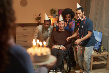 Full length portrait of Birthday surprise for young man with disability friend bringing Birthday cake with candles