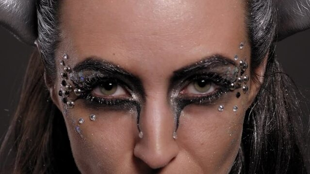 Close-up of a female model with silver skin and hands, with bright makeup with stones posing in the studio on a black background. A stern, cruel look.