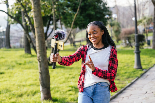 Smiling black afro woman vlogging outdoors with a phone and mic