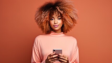 Beautiful Black woman with afro hair dyed in vibrant pink, holding mobile phone, isolated on beige...