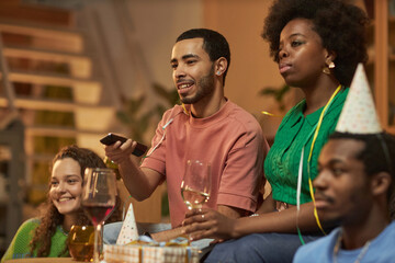Side view portrait of multiethnic group of adults watching TV or videos during party at home with...