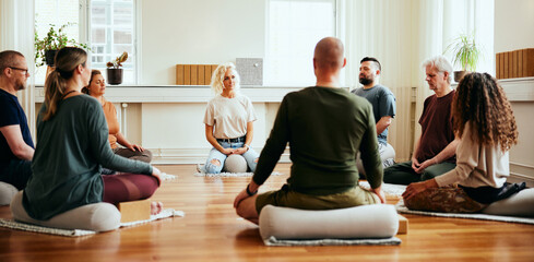 Yoga instructor teaching students meditation while they sit in n circles on a floor