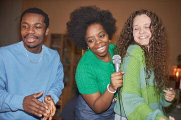 Diverse group of three adult people enjoying karaoke during house party and singing to microphone,...