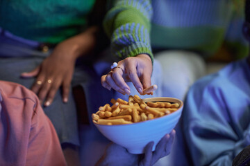 Close up of female hand holding popcorn bowl while watching movie in dark with friends