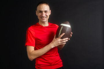 Young man dressed in casual street clothes holds a football, ready to throw a pass, isolated on...