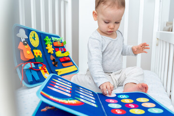 Baby playing with montessori quiet book sitting in a crib. Concept of smart books and modern educational toys