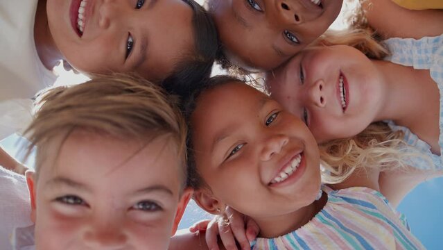 Portrait of group of smiling children joining arms in friendship looking down into camera together - shot in slow motion