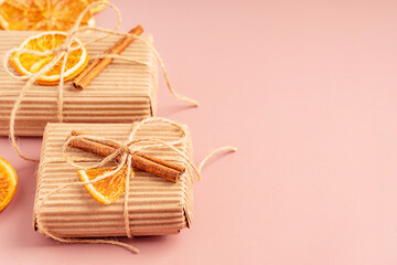 Sustainable gift boxes made of zero waste recycled carton material or paper tied with thread bow decorated with dried orange citrus fruit slice and cinnamon stick on brown background with copy space
