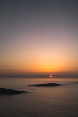 Spectacular sunset view from Monteferro's Rosa de los Vientos. Tranquil sea, clean horizon, Estelas islands' silhouettes, orange sky, and sun setting amid low grey clouds.