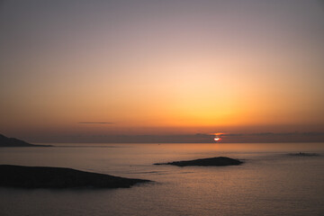 Captivating sunset view from Monteferro's Rosa dos Ventos. Tranquil seas, Estelas islands' silhouettes, and distant Cape Silleiro against an orange sky with the sun setting amid low grey clouds.