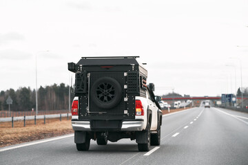 White pickup truck with a black box on the back driving down a highway. Truck has Off-Road package adds skid plates, mud flaps, all-terrain tires, and a suspension lift for better off-road capability. © AlexGo