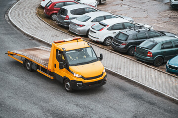A front view of an orange tow truck with a flatbed and a winch on a city street. Tow truck is about...