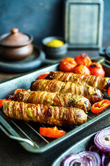 Grilled bacon wrapped sausages with tomatoes and onions on a baking tray