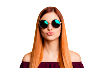 Portrait of red straight-haired attractive cute nice young girl, wearing sun glasses, blowing with pouted lips. Isolated over bright vivid yellow background