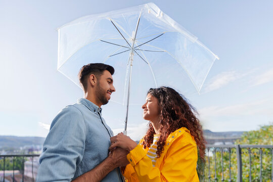 Romantic couple standing under umbrella on balcony