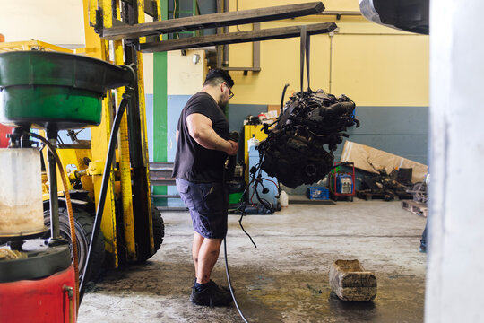 Mechanic examining engine hanging from forklift at workshop