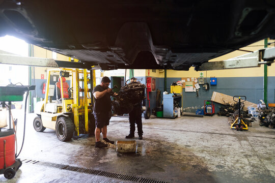 Auto mechanic colleagues working on machine part at workshop