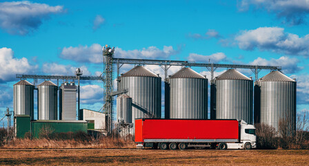 Semi-truck with red trailer in front of agricultural grain processing plant silos © Bits and Splits