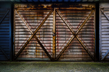 Old metallic garage door made of corrugated steel metal sheets locked with padlock