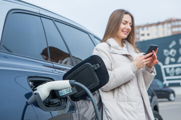 Young beautiful woman traveling by electric car having stop at charging station. Electric car...