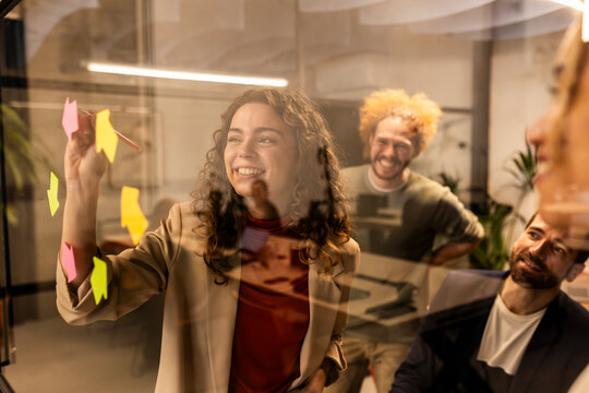 Smiling businesswoman doing brainstorming session with colleagues behind glass at office