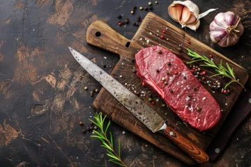 Foto op Canvas Raw uncooked top round beef steak on wooden cutting board with big kitchen knife and pepper on dark brown rustic stone background top view, cooking meat steak concept  © Straxer