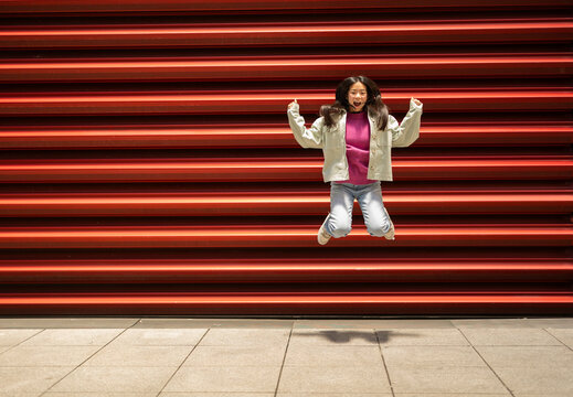 Cheerful young woman jumping in front of shutter
