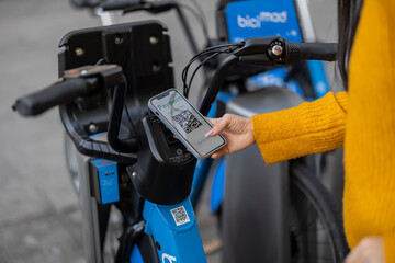 Woman scanning QR code through smart phone and renting electric bicycle