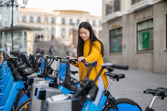 Smiling young woman renting electric bicycle in city