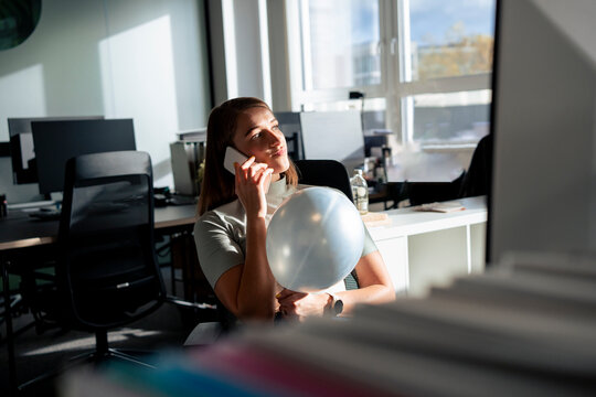 Young businesswoman holding balloon and talking on smart phone in office