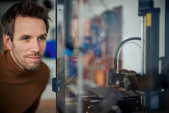 Engineer looking at 3d printer inside glass cabinet at workshop