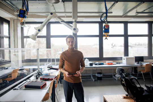 Confident engineer holding tablet PC at workshop