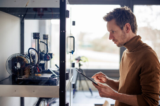 Engineer examining 3d printer machine through tablet PC at workshop
