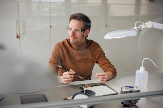 Thoughtful engineer working with soldering iron at workshop