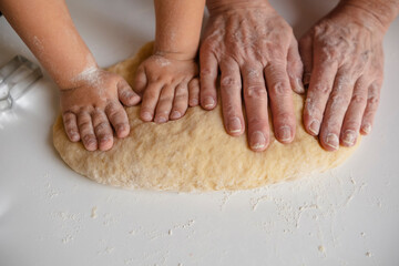Hands of grandmother and grandson kneading dough at home