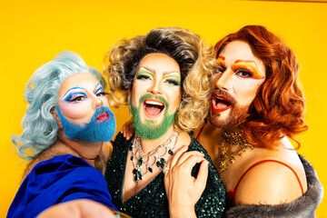 POV of three cheerful drag queens taking a selfie against yellow background