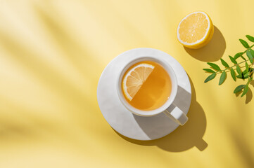 Herbal tea with lemon in a white cup on a yellow background with shadows.