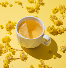 Herbal tea with immortelle and lemon in a white cup on a yellow background close up.