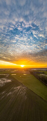This vertical portrait captures the grandeur of a sunset descending over farmlands. The sky, filled...