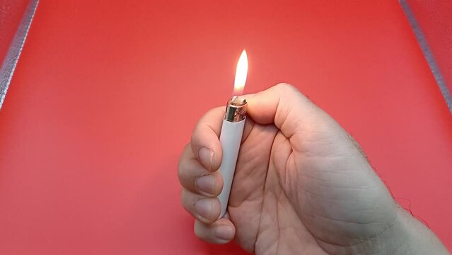 Lighter in man's hand. Close-up hand lights a lighter with sparks on a red background. 
