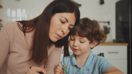 Mother attentively assists her young son with creative task at home, moment of family bonding. Tender moment of attentive parenting at home