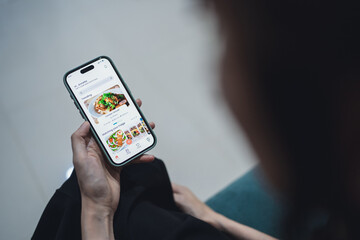 Top view of woman using mobile smart phone while order food delivery at home. Back view of young woman using food delivery app with mobile phone to order lunch.