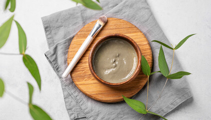 Organic cosmetic with blue clay on a wooden board with brush, branch and napkin on a light background.
