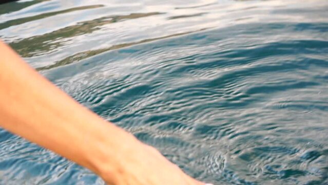 Woman hand sea. Close-up Happy Woman gently caresses water surface at sunset in a warm, golden evening by the sea or lake. Slow-motion Concept of happiness, boat life and holidays in exotic places