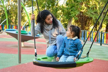 Latin mother playing with her son on a swing in a park. Latin family.