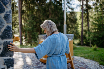 Fototapeta premium Happy young woman standing in garden near cottege and enjoying cup of morning coffee on summer vacation in mountains.