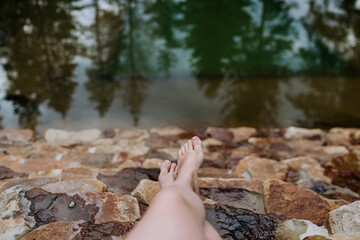 Young woman legs on stone stairs in natural pond during summer vacation in mountains.